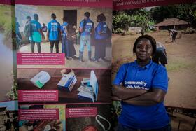 Bernadette Thomas a Community Health Worker from Bonthe District of Sierra Leone poses next to a photo exhibition about the challenges she and her colleagues face in the course of their work.