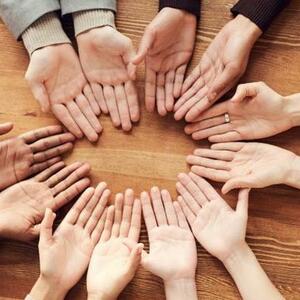 Image of many hands in a circle on a table. The hands are all facing palms up.