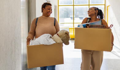 Young female students moving into student accommodation. Carrying belongings in boxes.