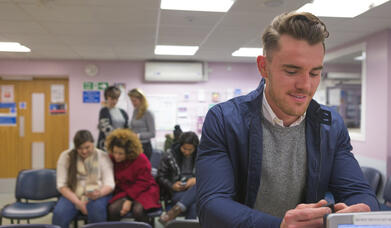 A horizontal image of a man in a doctor's clinic smiling at the receptionist booking him in for a medical check. He looks very cheerful and positive.