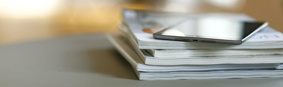 Gray digital tablet on a stack of magazines on a table