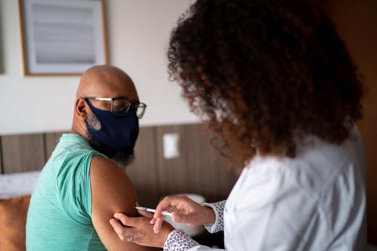 Doctor vaccinating a man wearing face mask stock photo