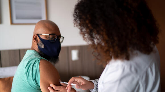 Doctor vaccinating a man wearing face mask stock photo