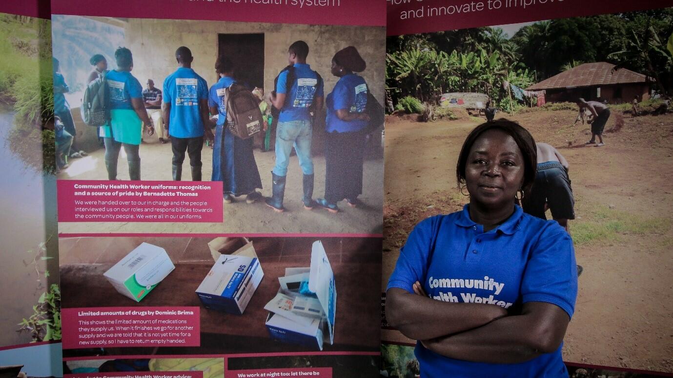 Bernadette Thomas a Community Health Worker from Bonthe District of Sierra Leone poses next to a photo exhibition about the challenges she and her colleagues face in the course of their work.
