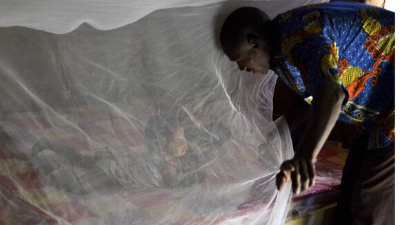 A father putting his daughter under a bednet in Burkina Faso - Photo credit: Jed Stone